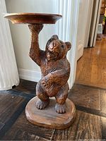 Front angle of carved wood side table shaped as a bear holding up a round tray, showing detail of carving and wood tones.