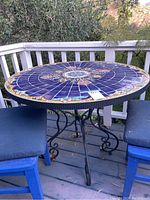 Full view of round table on deck showing blue mosaic top and metal base, surrounded by chairs