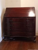 Wood secretary desk closed, showing dark wood with scratches and peeling finish on the drop-front and drawer fronts. Carved claw feet visible.