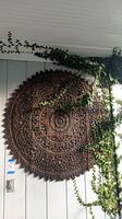 Full front view of round carved wood wall hanging mounted on exterior siding with ivy