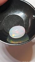 Oval white Ethiopian opal gemstone on black surface showing translucent body and color plays.