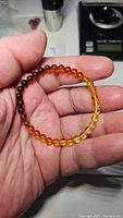 Close-up photo of a natural amber bracelet held in hand, showing smooth beads with a dark to light amber color gradient.