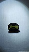 Oval-cut green tourmaline gemstone on white textured background under bright spotlight, clearly showing stone's color and cut.