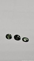 Photo of three oval cut mint green sapphires placed on a white background showing the color and shape.
