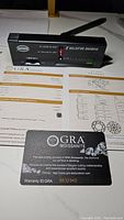 Photo showing diamond tester indicating moissanite authenticity alongside GRA warranty card and grading report.