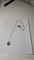 Full view of the necklace laid flat on white paper showing chain and pendant with deep red garnet gemstone.