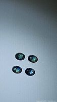 Four oval-cut blue-green sapphires spread on a white background under lighting, showing color and clarity.