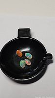 Four oval cabochon opal gemstones displayed in a black small round dish: three showing bright multicolor play-of-color typical of crystal opals and one brownish-red opal.