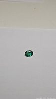 Oval cut emerald gemstone placed on white paper, showing rich green color and oval shape