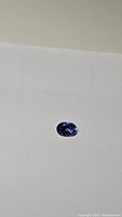 Close-up photo of a single oval cut tanzanite gemstone on a white background showing its color and cut details.