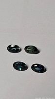 Four natural multicolored oval sapphires in blue and green colors on white background.