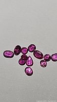 Twelve natural untreated rubies displayed on a white background showing variation in cut and color.