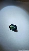 Close-up photo of oval-shaped sapphire gemstone highlighting its deep green color with blue tints under focused light.