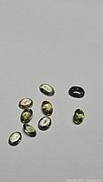 Nine small oval cut natural sapphires in various fancy light colors including light purple, green, and yellow hues, arranged on a white background.