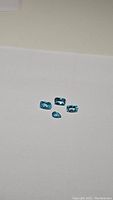 Four natural Paraiba blue apatite gemstones on a white background showing their cuts and color.