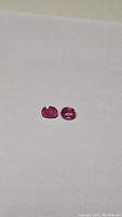 Two oval cut pink sapphire gemstones placed on a white background, showing color and clarity