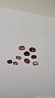 Parcel of nine natural pink tourmaline gemstones on a white background, varying in size and shape.
