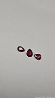 Three untreated pear-shaped deep red spinel gemstones from Myanmar on a plain background showing clarity and color.