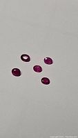 Five oval faceted rubies in varying shades of deep red and pink on a white background in natural light.
