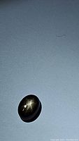 Oval cabochon black star sapphire showing the characteristic 6-ray star effect.