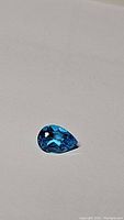 Pear-shaped Swiss Blue Topaz gemstone on white background, showing deep lagoon blue color and facets.