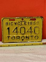 Yellow metal 1950 Toronto bicycle license plate with embossed black numbers and lettering showing wear consistent with age.