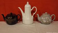 All three tea pots displayed together against an orange backdrop.