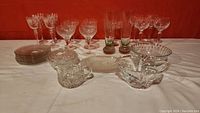 Photo showing the full assortment of glassware including stemware, plates, covered dish, sugar bowl, and decorative bowl on white cloth against red background.