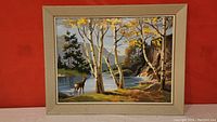 Full view of framed paint by number artwork showing deer at a pond with birch trees and rocky cliff background.