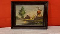 Framed oil painting showing a Dutch windmill, water, buildings and a duck, overall view of the lot.