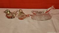 Photo showing two amber-tinted glass bird figurines and one clear glass whale calf figurine on a flat surface.