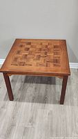 Front view of square rosewood coffee table with parquet pattern top on gray floor against beige wall