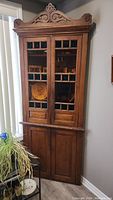 Full front view of wooden corner cabinet with carved crest and dual doors