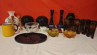 Full lot of vintage items arranged on a white surface with red background showing candle holders, glass bowls, folding screen and other decorative items.