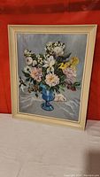 Framed oil painting showing the full artwork of flowers in blue vase by L. W. Higginson.