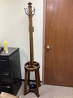 Full view of the antique wooden coat stand showing the tall central post with metal hooks at the top and four legs forming the base.