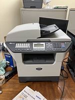 Full view of Brother MFC-8460N all-in-one printer photocopier fax machine with visible control panel and document feeder, placed on wooden floor with user manuals nearby.