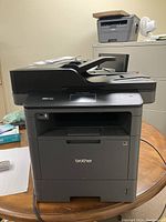 Full front and top view of Brother MFC-L5800DW printer sitting on wooden table with automatic document feeder and control panel visible.