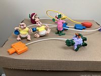 Five assorted vintage McDonald's character toys are shown, including two babies, Santa Claus figure, and two dinosaurs, one with fishing game accessory.