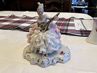 Front view of porcelain figurine showing the woman in a detailed white ruffled dress playing a mandolin, set on a decorated base.
