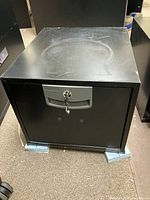 Closed black fire resistant filing cabinet with key lock visible on the drawer.