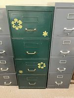 Front view of the green filing cabinet with yellow flower decals on the drawers, between two grey filing cabinets.