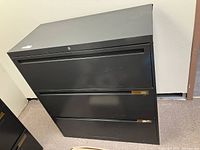 Front view of grey metal filing cabinet showing three closed drawers and overall structure.