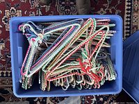 Blue plastic bin with colorful plastic woven wire hangers inside, showing various multi-colored braided plastic coatings.