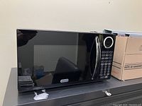 Closed black microwave with reflective door, stainless steel handle, keypad and dial on the right side.