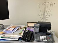 Photo showing three solar powered calculators, a black thank you card holder, a black handheld pencil sharpener, assorted pencils, and a large stack of papers and envelopes.