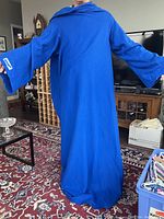 Full view of a blue Snuggie blanket worn by a person showing loose fit, long sleeves, and hood.