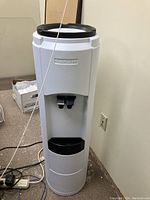Front view of the white water cooler with black drip tray and dual spigots.