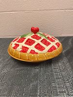 Side view of cherry pie ceramic dish showing lattice design, cherry details, and lid with heart-shaped cherry handle.
