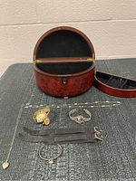 Wooden oval jewelry box open with black velvet interior and costume jewelry and wristwatches displayed in front